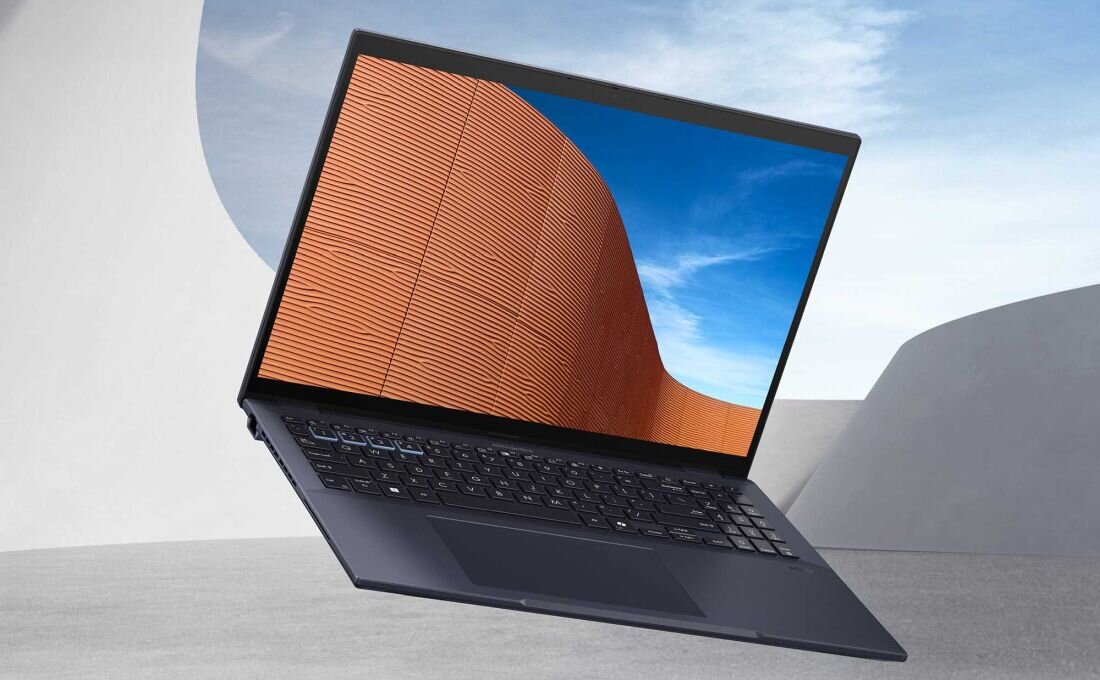 Laptop ASUS ExpertBook B5 w ciemnej obudowie z ekranem prezentującym abstrakcyjną, pomarańczową architekturę na tle błękitnego nieba, podkreślający elegancki design i jakość wyświetlacza w minimalistycznym otoczeniu .