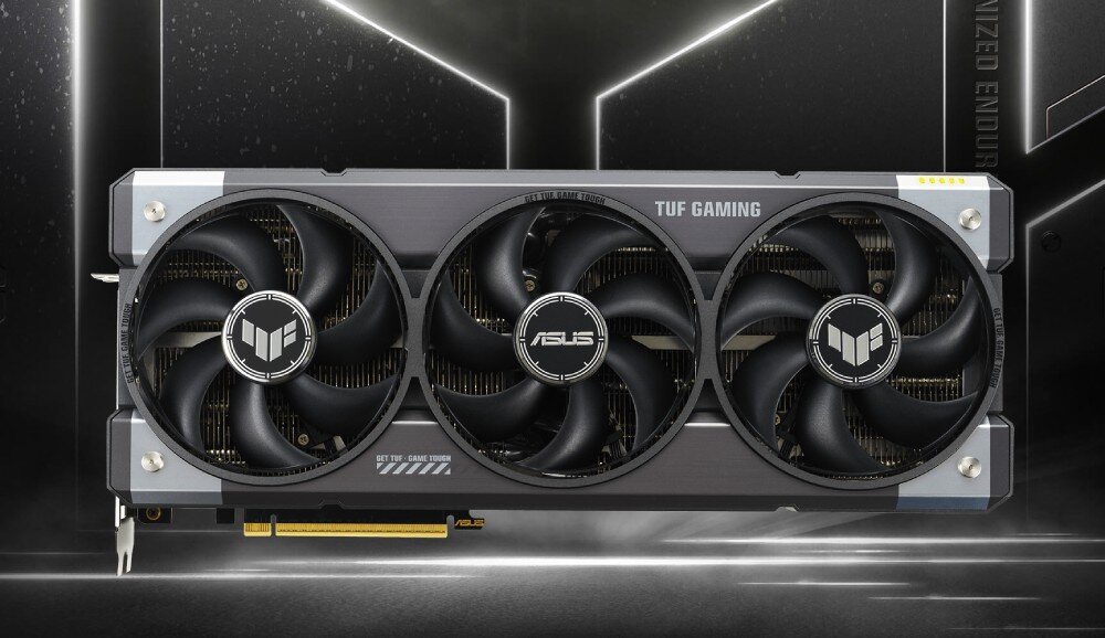 Karta graficzna ASUS GeForce RTX 5090 TUF Gaming 32GB Grafika przedstawia kartę graficzną w wersji TUF Gaming o industrialnym wyglądzie. Na wentylatorach widoczne są logotypy producenta i serii