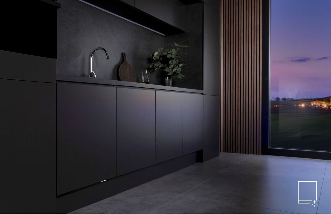 Nowoczesna kuchnia z ciemnymi szafkami i zlewem, obok którego stoją dekoracje. Przez duże okno widać wieczorny krajobraz z oświetlonymi budynkami.