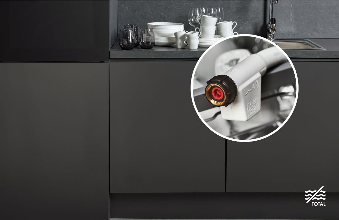 Kuchnia z ciemnymi szafkami, na blacie stoją białe naczynia i szklanki. W prawym dolnym rogu widoczne jest logo \'TOTAL\'.