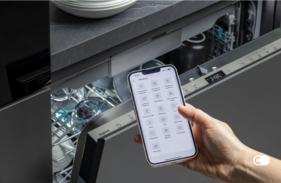 Osoba trzyma smartfon z aplikacją do zarządzania urządzeniami, przed otwartą zmywarką marki Hisense. Na panelu zmywarki widoczny jest wyświetlacz z liczbą \'2:39\'.