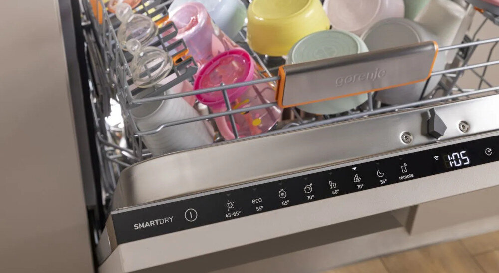 ZMYWARKA GORENJE GV693A65AD Na zdjęciu widoczny jest górny kosz zmywarki wypełniony kolorowymi dziecięcymi butelkami i pojemnikami. Na froncie urządzenia widać panel sterowania z czasem 1:05 oraz przyciskiem SmartDry program sterylizacja płukanie gorąca woda 70°C eliminacja bakterii wysoka higiena profesjonalny proces