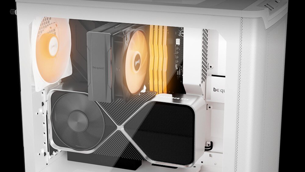 Obraz przedstawia wnętrze białej obudowy komputerowej z widocznymi komponentami, takimi jak wentylatory z pomarańczowym podświetleniem i karta graficzna. Na obudowie widoczne jest logo \'be quiet!\'.
