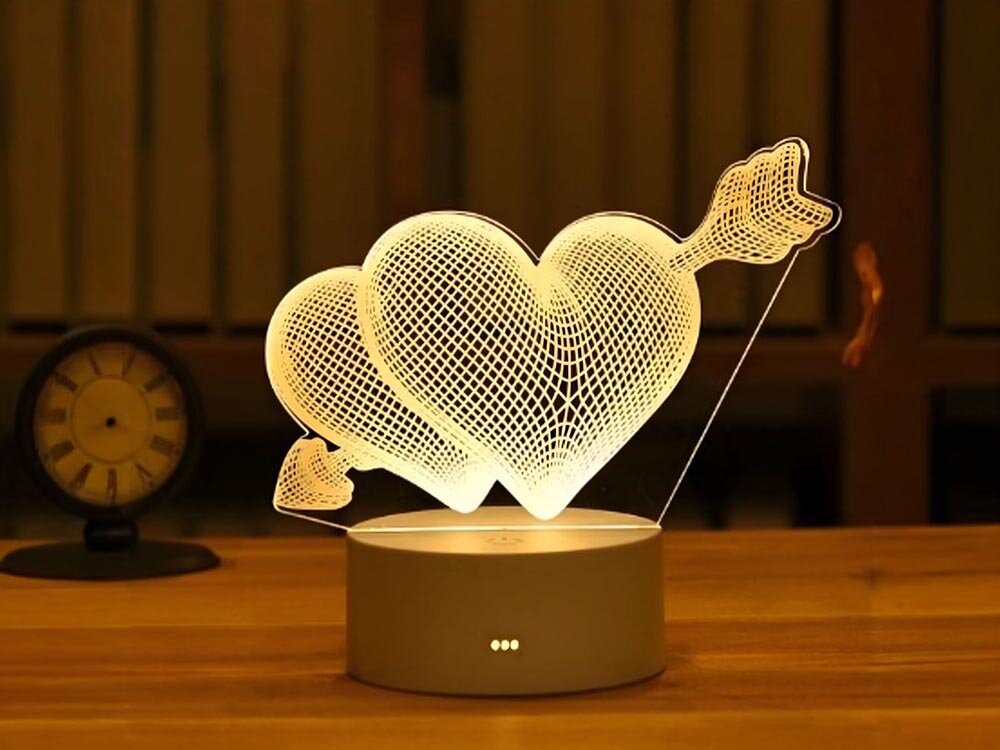 Lampka nocna EXTRALINK Przebite serca 3D EX.24107 USB, LED, biel, relaks, oszczędność, Lampa LED 3D serca ze strzałą obok zegara na stoliku wieczorem.