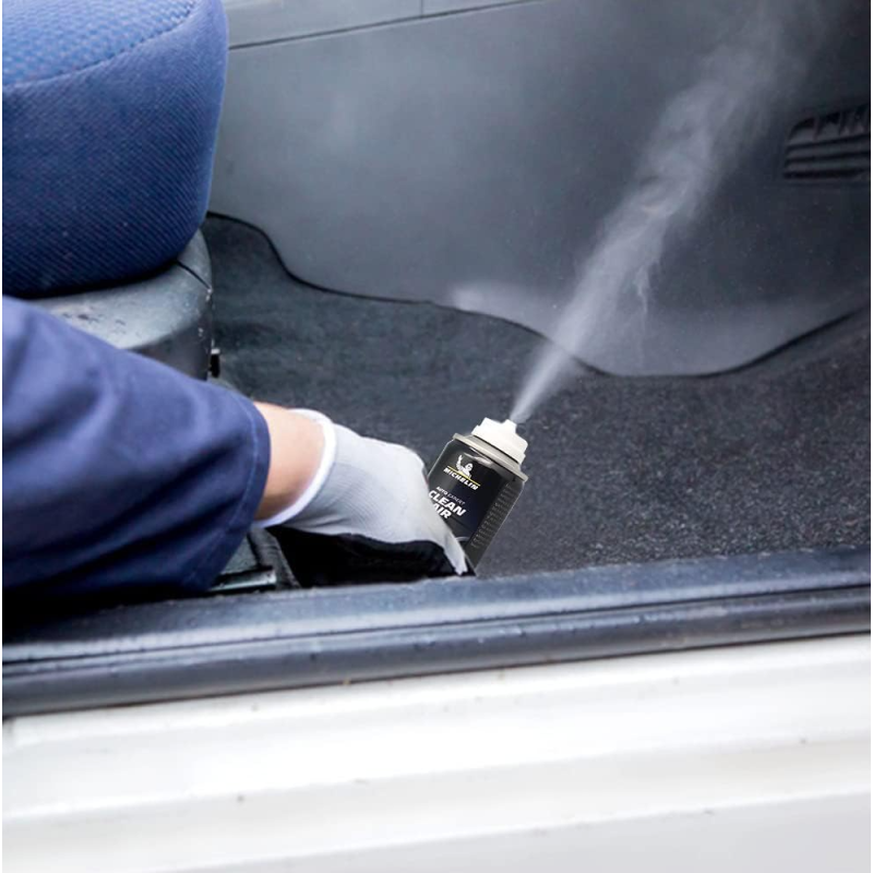 Osoba w rękawiczce trzyma puszkę z napisem \'CLEAN AIR\', z której wydobywa się mgiełka. Puszka znajduje się wewnątrz pojazdu na wykładzinie podłogowej.