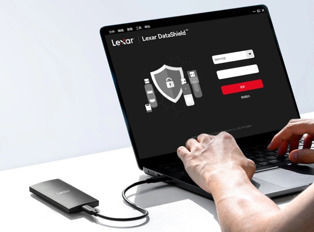 Dysk LEXAR SL300 Laptop z wyświetlonym oprogramowaniem Lexar DataShield i podłączonym dyskiem na biurku