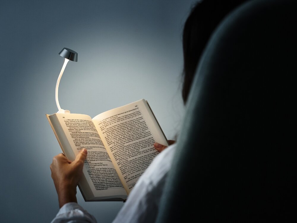Lampka LED LEXON Mimi Aluminium
osoba trzyma książkę wpięta lampka do codziennego oświetlenia stylowy design praktyczność elastyczne ramię klips na książce biurku półce do domu biura w podróży dobre światło