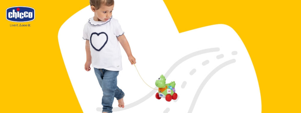 Zabawka interaktywna CHICCO Baby Sense & Focus Mój pierwszy Dino 00012119000000 biało żółte tło dziecko wyprowadza zielonego dinozaura na kółkach na spacer trzyma sznurek 50-centymetrowy sznurek maluch może zabrać swojego dinozaura na spacer wspiera rozwój motoryki dużej zachęcanie do chodzenia ciągnięcia i aktywnego poruszania się dla maluchów, które zaczynają stawiać pierwsze kroki i chcą bawić się w ruchu