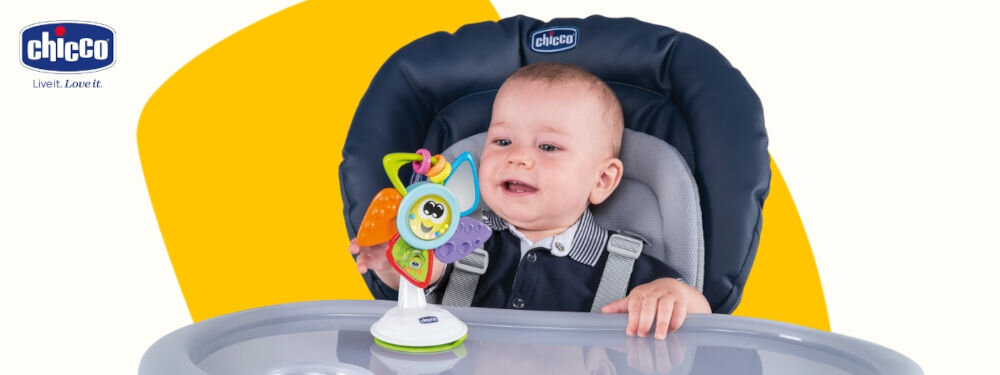 Zabawka edukacyjna CHICCO Baby Senses Kolorowy wiatraczek 00009710000000 uśmiech dziecka biało żółte tło maluch siedzi w krzesełku przyczepiona kolorowa zabawka maluch bawi się zabawką