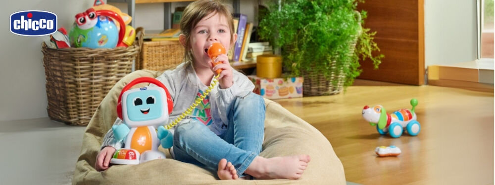 Zabawka edukacyjna CHICCO Happy Music Śpiewający robot Robit 00011853000000 dziecko siedzące z zabawką robota świecący brzuch zabawki przyciski na obudowie dziewczynka trzyma w ręku pomarańczowy mikrofon i śpiewa Śpiewanie do mikrofonu wybór różnych gatunków muzycznych tworzenie zabawnych efektów głosowych wsparcie rozwoju mowy oraz wyobraźni motywuje do naśladowania dźwięków rozwój zdolności językowych i umiejętności komunikacyjnych stymulacja poczucia rytmu i koordynacji słuchowej