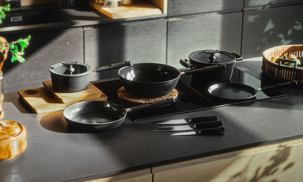 Patelnia FISKARS Hard Face 1075458 24 cm do każdej kuchni czarne garnki i patelnie stoją na płycie obok leżą noże  