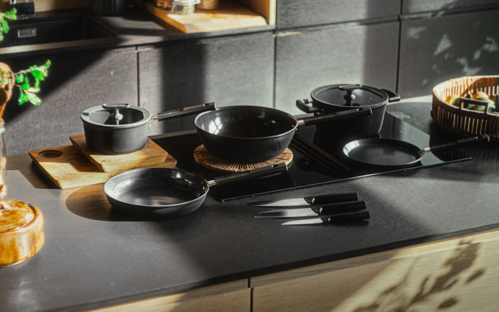 Patelnia FISKARS Hard Face 1075520 28 cm do każdej kuchni czarne garnki i patelnie stoją na blacie obok leżą noże  