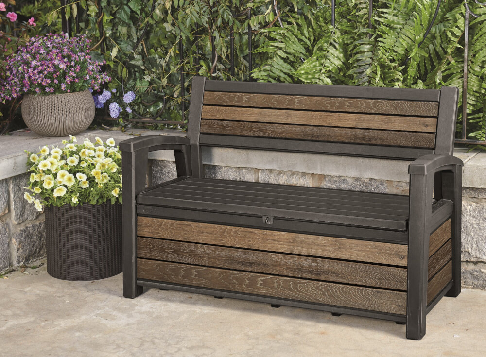 Ławka ogrodowa KETER Deco Garden Bench Brązowy ławka stoi na podłodze w tle rośliny odpoczynek na świeżym powietrzu relaks mebel ogrodowy funkcja schowka funkcja siedziska