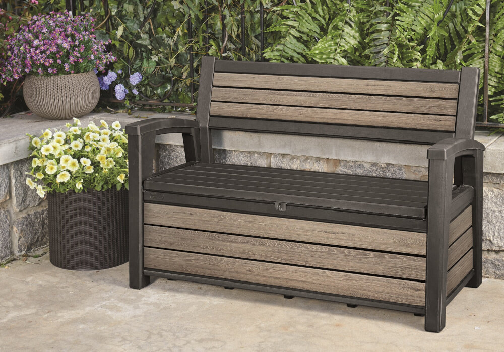 Ławka ogrodowa KETER Deco Garden Bench Popielaty ławka stoi na podłodze w tle rośliny odpoczynek na świeżym powietrzu relaks mebel ogrodowy funkcja schowka funkcja siedziska
