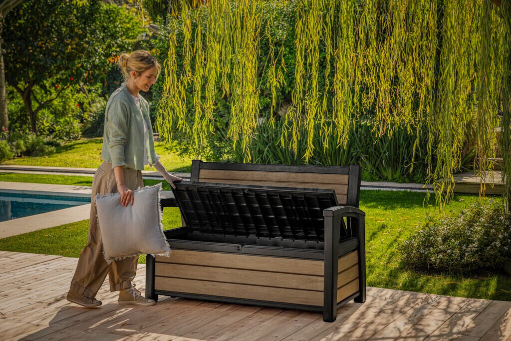 Ławka ogrodowa KETER Deco Garden Bench Popielaty, 227 litrów, wymiary, schowek, organizacja, Kobieta chowa akcesoria ogrodowe do schowka w ławce Deco Garden Bench.