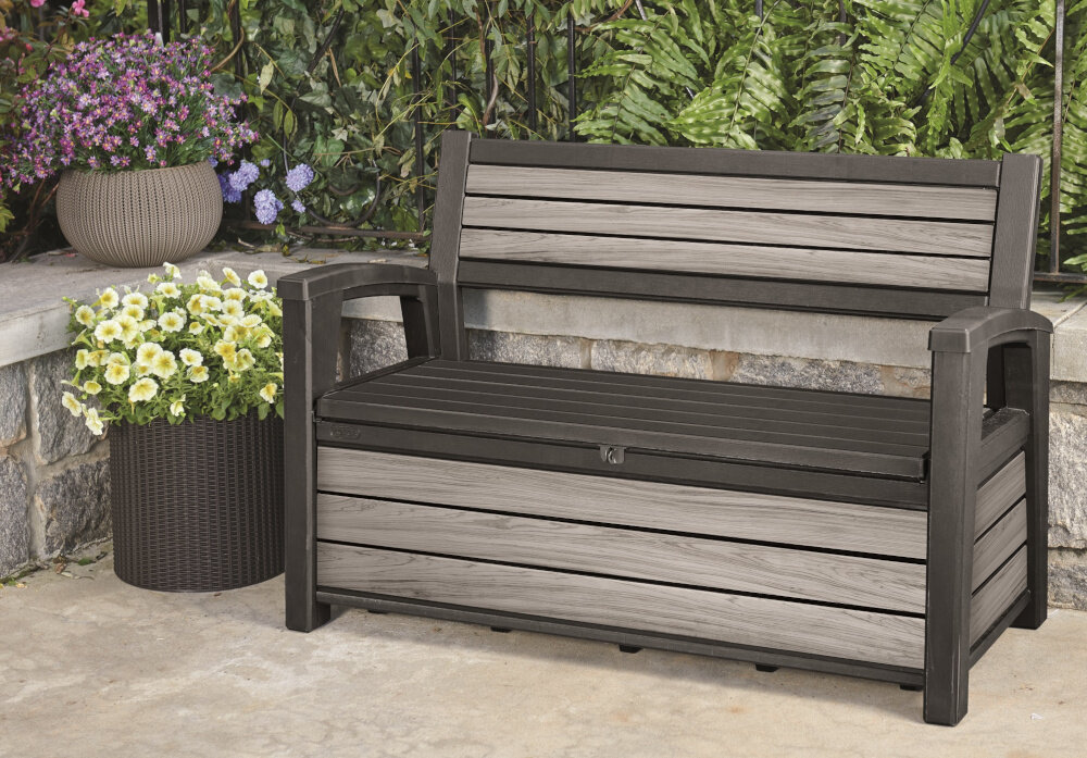Ławka ogrodowa KETER Deco Garden Bench Szary ławka stoi na podłodze w tle rośliny odpoczynek na świeżym powietrzu relaks mebel ogrodowy funkcja schowka funkcja siedziska