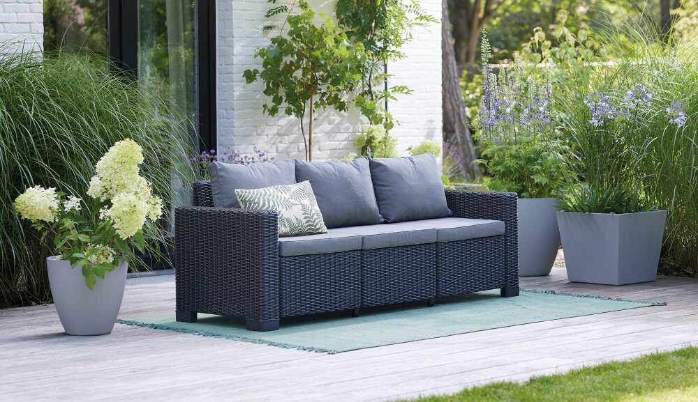 Sofa KETER California Brązowo-beżowy sofa na tarasie wśród roślin prosty montaż system JUST CLICK AND GO montaż na zatrzaski intuicyjny w obsłudze nie wymaga użycia dodatkowych narzędzi Intuicyjny system łączenia szybkie i proste złożenie sofy