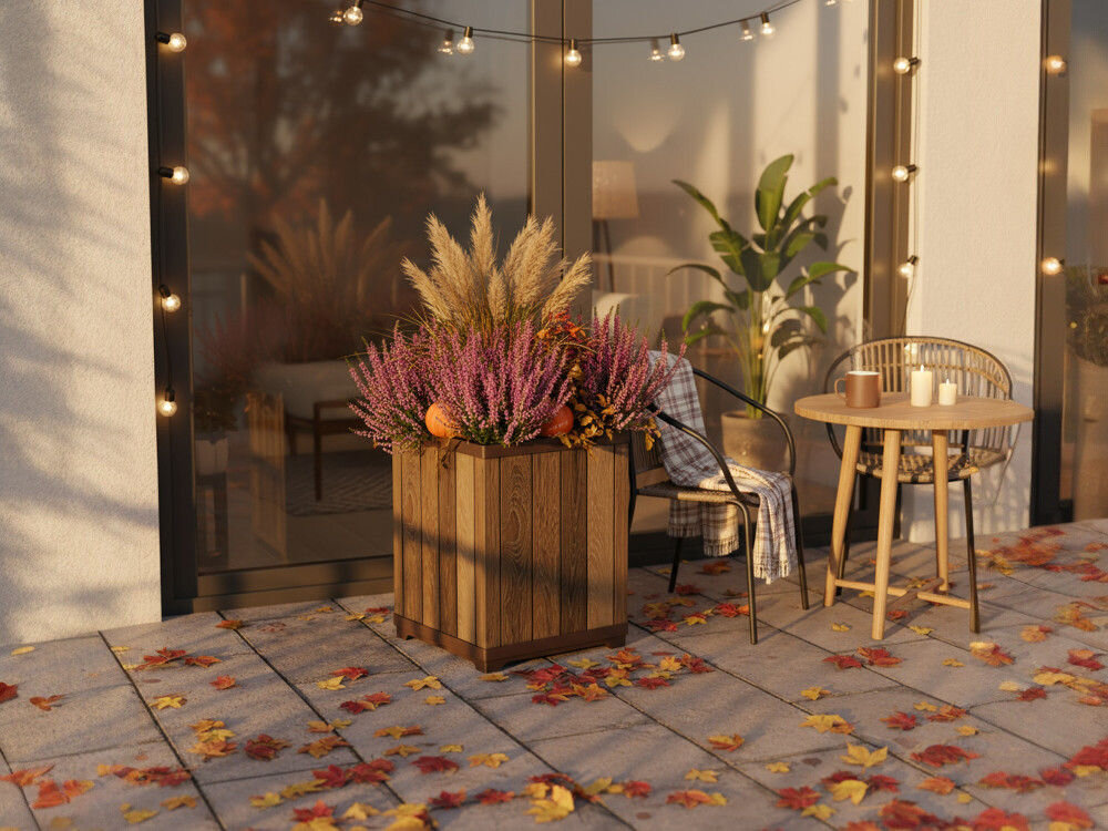 Na tarasie znajduje się drewniana doniczka z różnorodnymi roślinami ozdobnymi. Obok stoi stolik z krzesłem, a na podłodze leżą kolorowe liście.