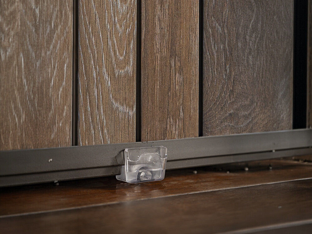 Obraz przedstawia drewnianą powierzchnię z pionowymi panelami, z przezroczystym elementem zamocowanym na dolnej krawędzi. Panele mają wyraźną teksturę drewna w odcieniach brązu.