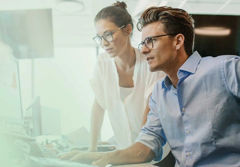 Komputer MSI Cubi NUC 13MQ-062EU Dwie osoby w biurze wpatrzone w ekran komputera, kobieta stoi obok siedzącego mężczyzny, rozbudowa modernizacja zdalne zarządzanie