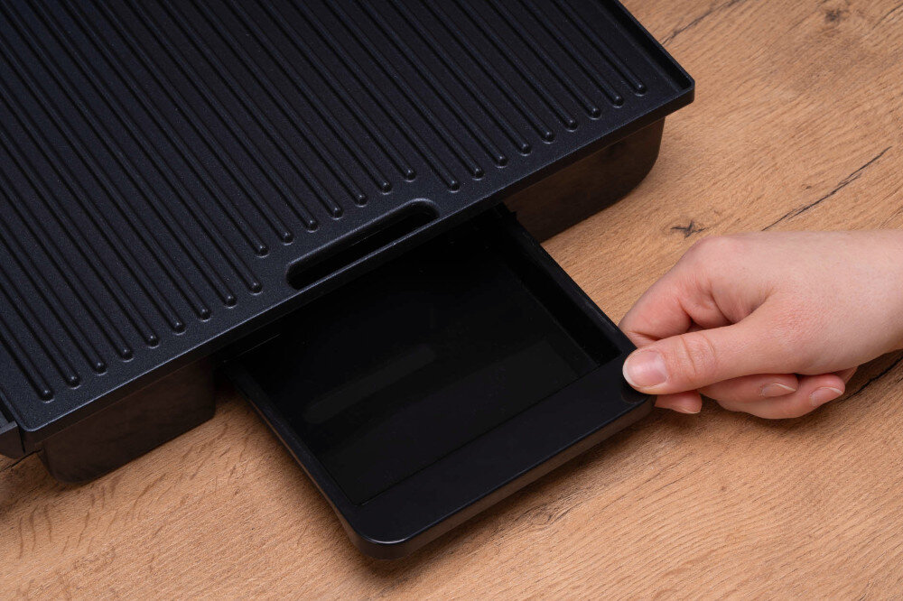 Grill elektryczny GÖTZE & JENSEN GL500X zbliżenie na tackę ociekową osoba wyciąga ją z grilla wyjmowana tacka ociekowa czystość