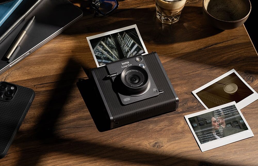 Aparat FUJIFILM Instax Wide Evo na stole z odbitkami