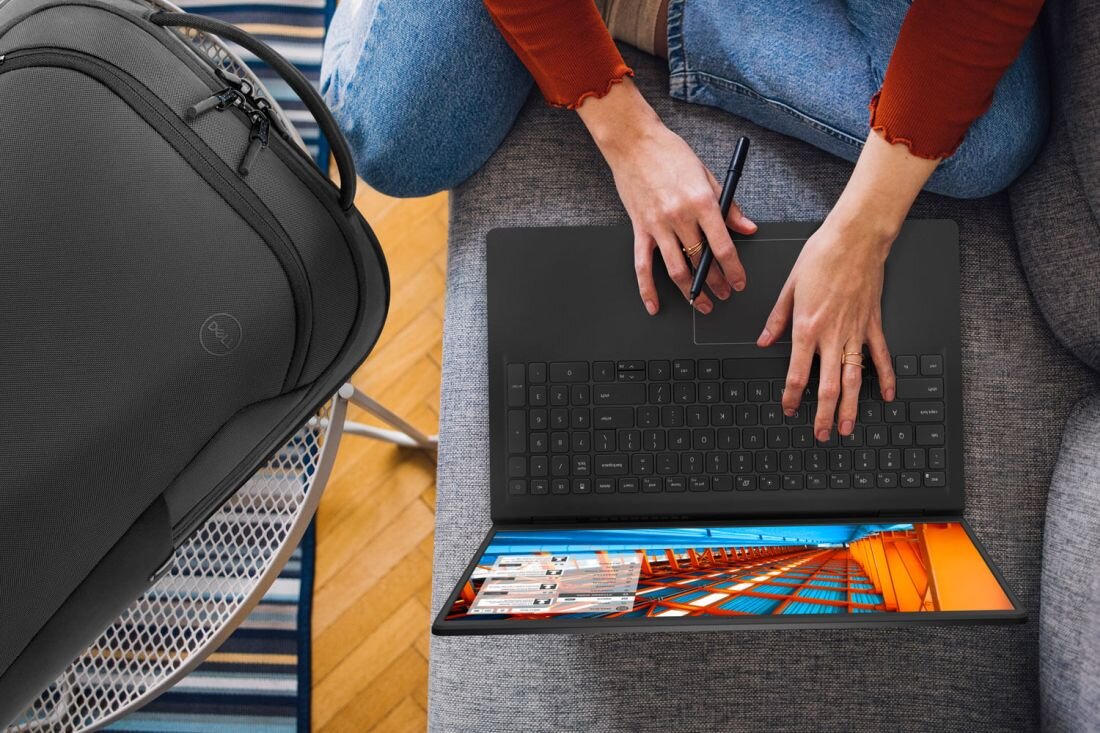 Kobieta pisze na laptopie DELL Inspiron 3530, obok niej stoi walizka na kanapie. - Błyskawiczne uruchamianie, Czujnik otwarcia pokrywy