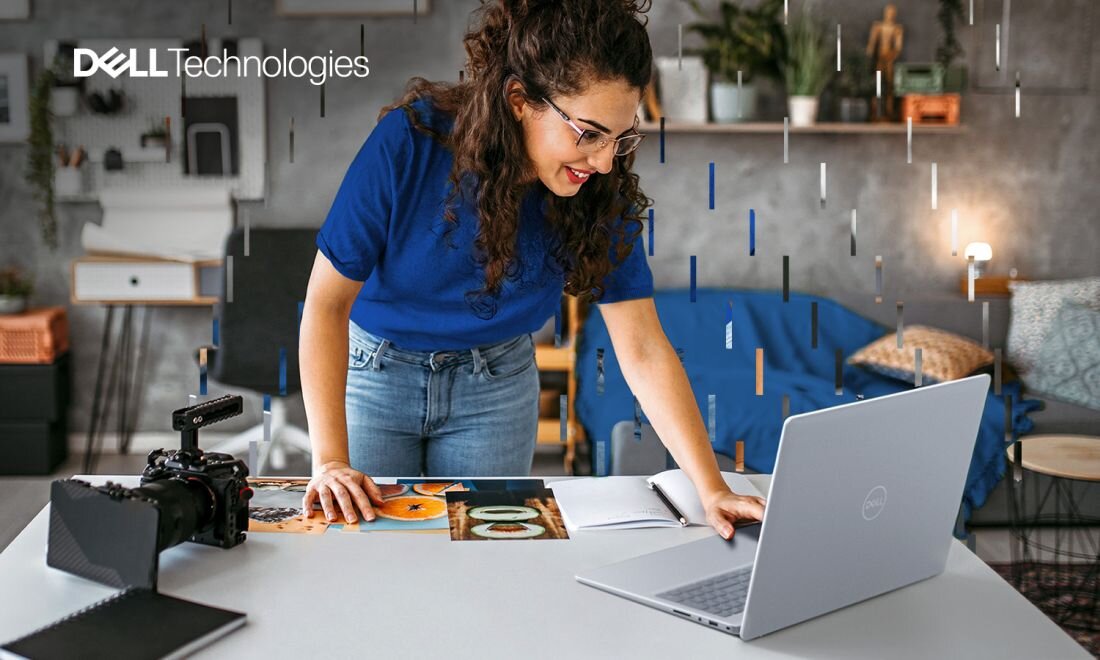 Kobieta pracująca przy biurku na laptopie Dell Inspiron 5640, na stole aparat fotograficzny, zdjęcia i notatnik, w tle domowe studio, logo Dell Technologies w lewym górnym rogu.