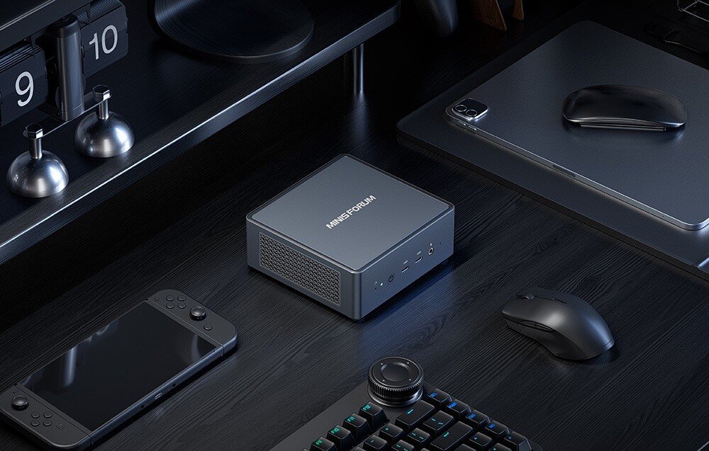 Komputer MINISFORUM Venus UM790 Pro Srebrna miniaturowa stacja dokująca MINISFORUM na ciemnym biurku obok myszki, klawiatury i konsoli.