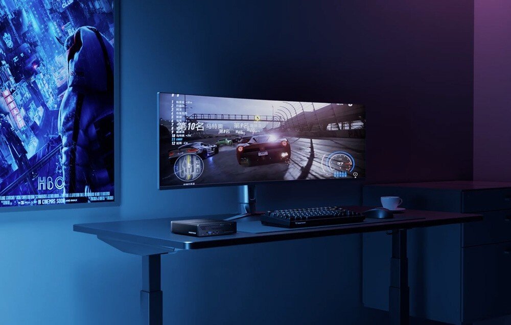 Komputer MINISFORUM MS-01-S1390 Mini PC na biurku obok panoramicznego monitora z grą wyścigową, klawiatury i myszki w ciemnym, nowoczesnym pokoju.