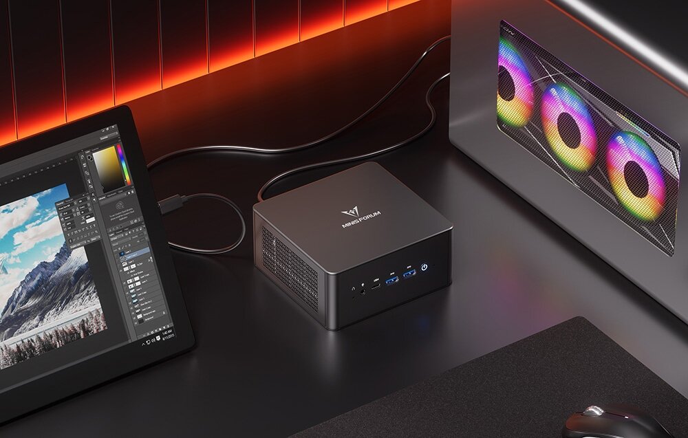 Komputer MINISFORUM EliteMini UM890 Pro Minisforum na stanowisku kreatywnym obok tabletu graficznego i zewnętrznej karty graficznej z podświetleniem RGB.