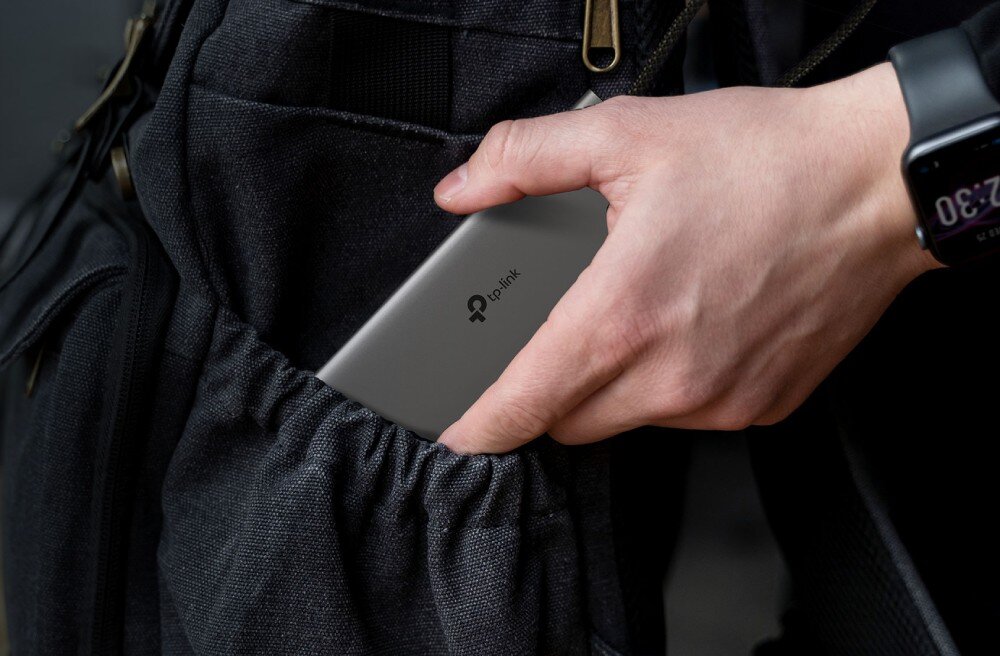 Hub TP-LINK UH9120C Męska dłoń wkładająca smukły, szary adapter do bocznej kieszeni czarnego płóciennego plecaka