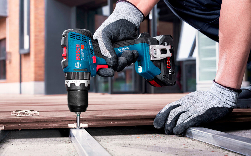 Wiertarko-wkrętarka BOSCH Professional GSB 18V-65 06019N3300 podest osoba trzyma wiertarko-wkrętarkę w dłoniach przykręca śrubę do drewnianej konstrukcji wkręcanie wkrętów w drewnie wiercenie w metalu oraz murze funkcja udaru jedno urządzenie pozwala wykonać więcej prac szybciej i przy mniejszym bałaganie