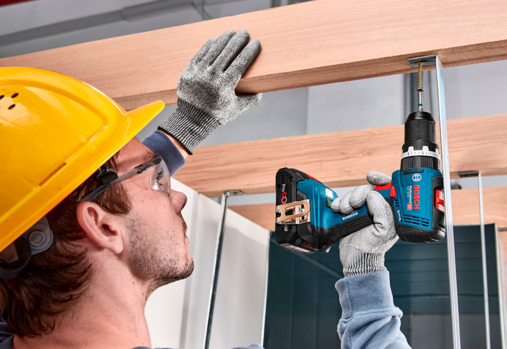 Wiertarko-wkrętarka BOSCH Professional GSB 18V-65 06019N3300 pomieszczenie drewniana konstrukcja osoba trzyma wiertarko-wkrętarkę w dłoniach przykręca śrubę do konstrukcji funkcja KickBack Control wykrywa nagłe zablokowanie wiertła lub bitu i automatycznie zatrzymuje silnik zmniejsza ryzyko utraty kontroli redukuje obciążenie nadgarstka sprzyja stabilniejszemu prowadzeniu urządzenia zwiększa bezpieczeństwo