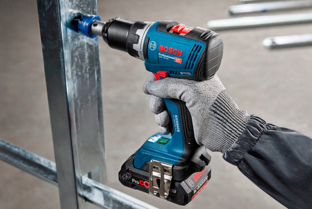 Wiertarko-wkrętarka BOSCH Professional GSR 18V-65 06019N3200 pomieszczenie metalowy profil osoba wierci dziurę w profilu podwójne oświetlenie robocze w stopie i pod uchwytem wiertarskim doświetla miejsce pracy strumień światła obejmuje zarówno bezpośrednio linię wiercenia, jak i otoczenie precyzyjne prowadzenie wiertła lub wkręta