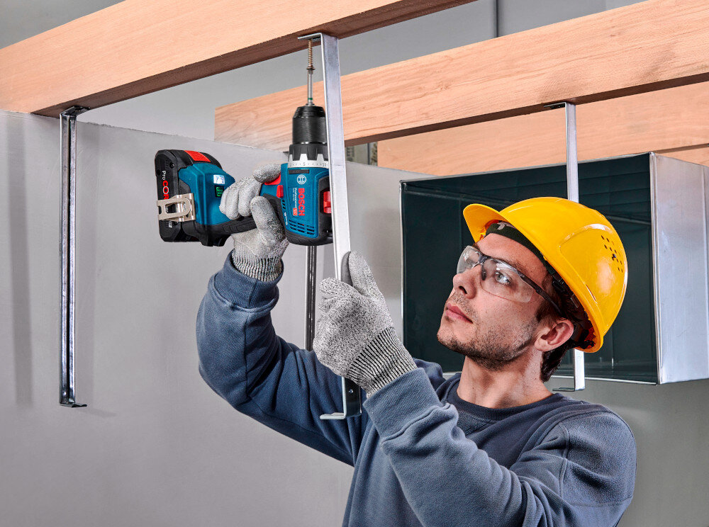 Wiertarko-wkrętarka BOSCH Professional GSR 18V-65 06019N3203 pomieszczenie drewniana konstrukcja osoba trzyma wiertarko-wkrętarkę w dłoniach przykręca metalowy hak do konstrukcji moment obrotowy 31/63/76 Nm dopasowanie siły pracy do różnych zadań dwubiegowa przekładnia z prędkością 0–550 oraz 0–2.100 obr./min zwiększa się zakres zastosowań i łatwiej dobrać parametry do konkretnego materiału