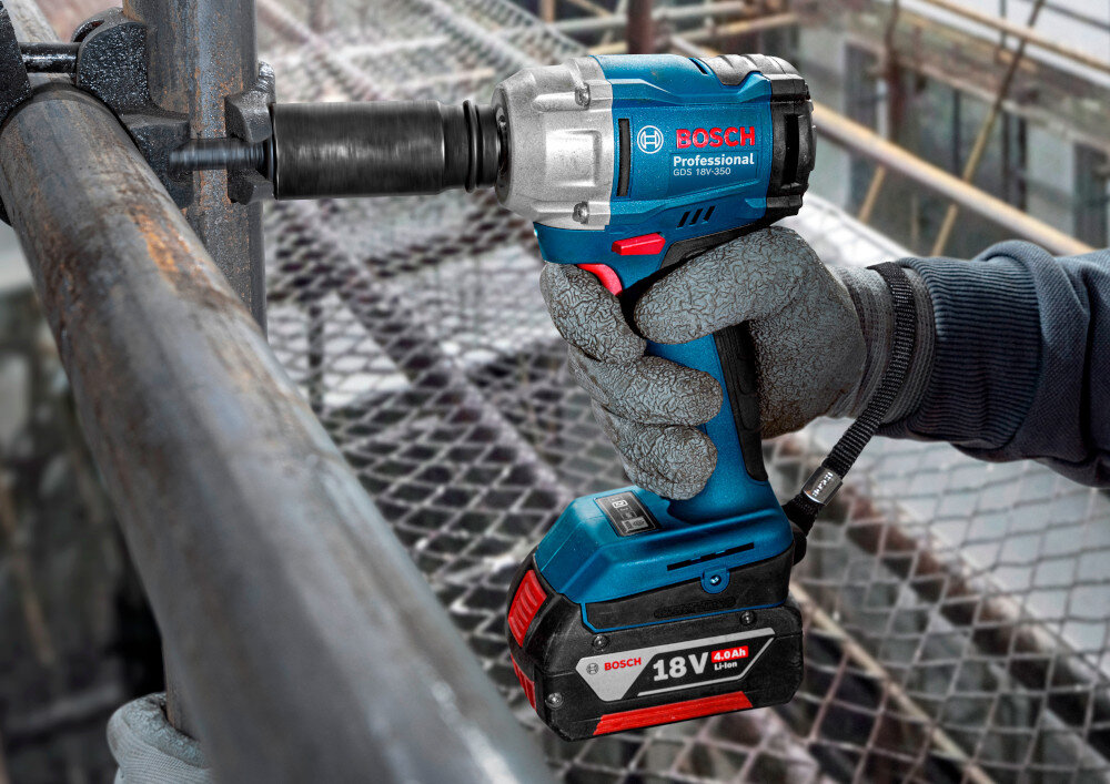 Klucz udarowy BOSCH Professional GDS 18V-350 06019M5021 plac budowy osoba dokręca śruby na metalowej konstrukcji zbliżenie na sam klucz obudowę konstrukcja odporna na uszkodzenia ergonomiczny kształt rękojeści antypoślizgowa powłoka waga około 1,1 kg bez akumulatora większy komfort i lepsza kontrola narzędzia