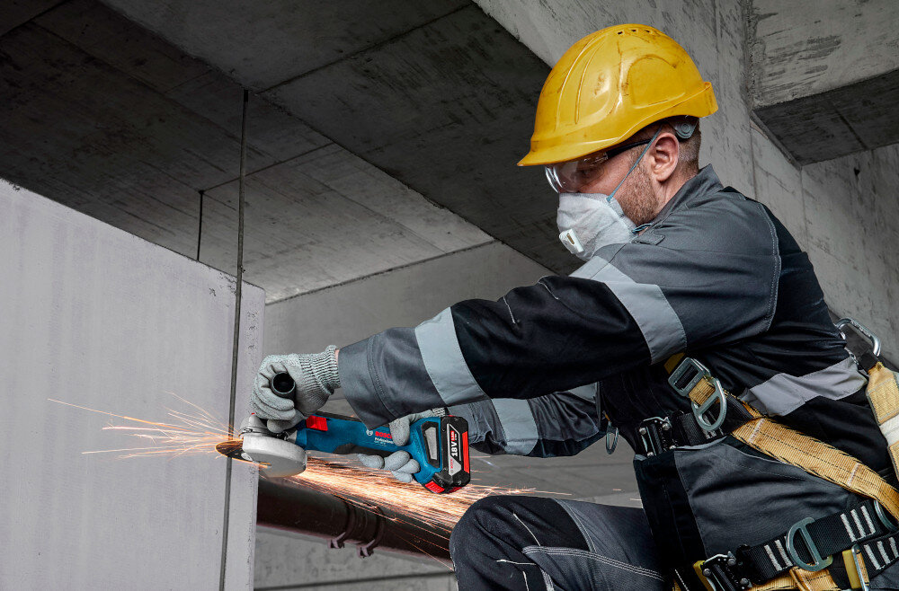 Szlifierka kątowa BOSCH Professional GWS 18V-8 06019N9001 osoba trzyma szlifierkę w dłoniach tnie metalową rurkę wszechstronne narzędzie dla majsterkowiczów bezpieczne użytkowanie kontrola potężne obroty