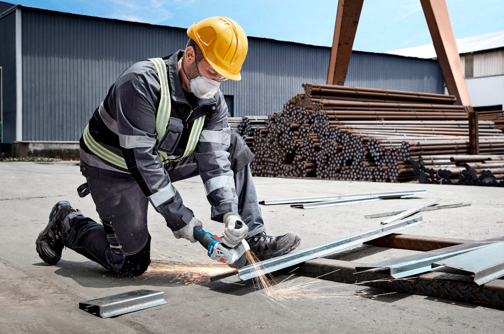 Szlifierka kątowa BOSCH Professional GWS 18V-8 06019N9003 osoba trzyma szlifierkę w dłoniach tnie metalowy element wszechstronne narzędzie dla majsterkowiczów bezpieczne użytkowanie kontrola potężne obroty