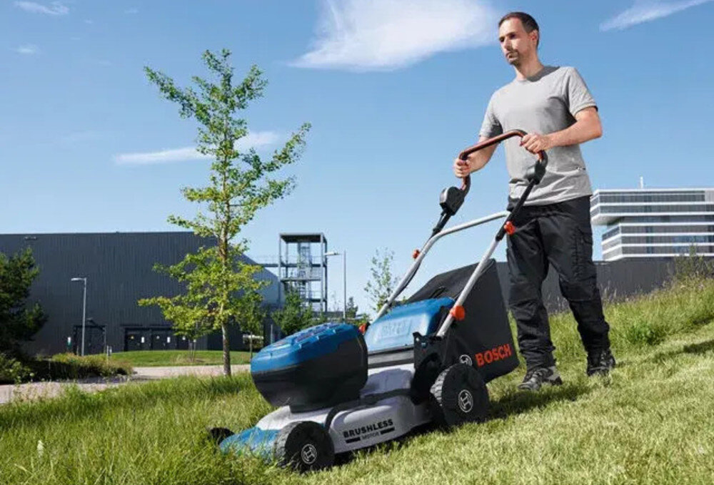Kosiarka akumulatorowa BOSCH Professional GRA 18V2-46 06008C8000 trawnik w tle budynki osoba kosi trawę wydajna pielęgnacja trawnika pielęgnacja dużych trawników zasilanie akumulatorowe