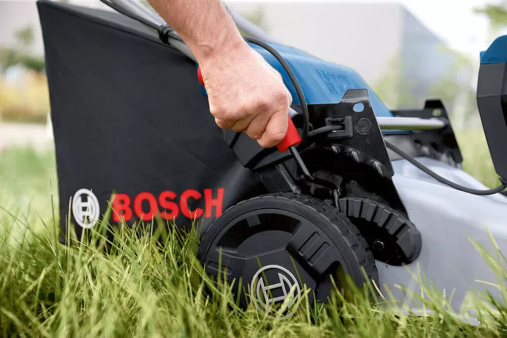 Kosiarka akumulatorowa BOSCH Professional GRA 18V2-46 06008C8000 trawnik zbliżenie na dźwignię do regulacji wysokości koszenia osoba reguluje wysokość sześciostopniowa regulacja wysokości w zakresie od 30 do 70 mm odbywa się płynnie regulacja za pomocą dźwigni umieszczonej obok tylnego koła