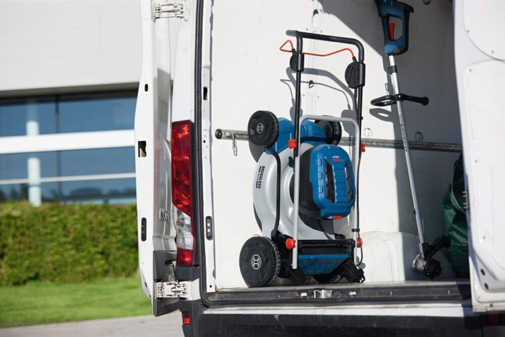 Kosiarka akumulatorowa BOSCH Professional GRA 18V2-46 06008C8000 złożona kosiarka umieszczona w samochodzie w tle budynek i rośliny składany uchwyt możliwość przechowywania w pozycji pionowej waga 27,7 kg stabilne podczas koszenia komfort i precyzja pracy