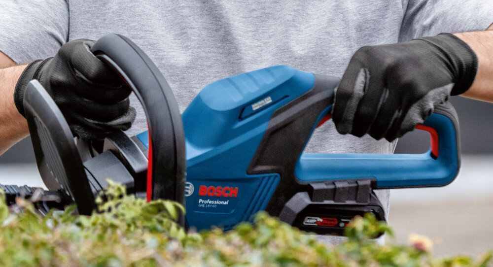 Nożyce do żywopłotu BOSCH Professional GHE 18V-50 06008C9500 akumulatorowe żywopłot zbliżenie na silnik osoba trzyma nożyce w dłoni bezzczotkowy silnik wysoka moc przy niższym zużyciu energii dłuższą pracę bez konieczności częstego ładowania akumulatora zwiększa żywotność urządzenia zmniejsza koszty eksploatacji stabilna wydajność