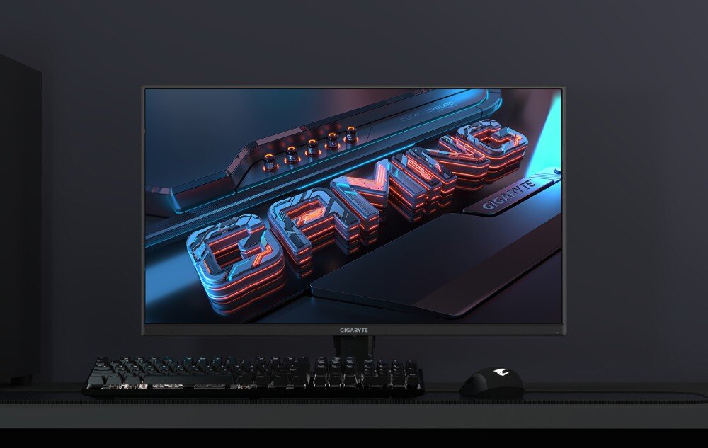 Monitor GIGABYTE GS27QA EU Monitor komputerowy wyświetlający trójwymiarowy napis „GAMING” w czerwono-niebieskiej kolorystyce, ustawiony na biurku obok klawiatury i myszy, opis