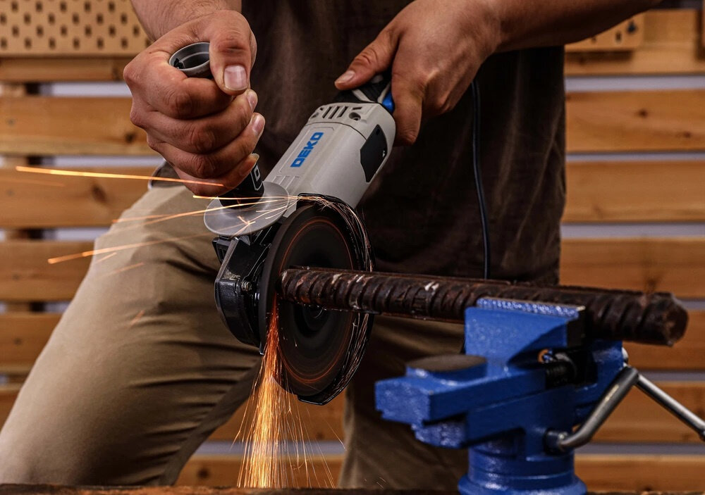 Szlifierka kątowa DEKO DKAG125XP110S osoba używa szlifierki szlifuje metalową rurkę iskry spod tarczy osłona tarczy bezpieczeństwo pracy klasy ochrony II współpracuje z tarczami o średnicy 125 mm można nią szlifować beton drewno tworzywa sztuczne tnie glazurę gres i inne materiały ceramiczne