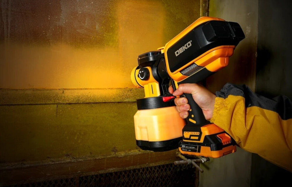 Pistolet natryskowy DEKO DKSG20K4 1200 ml osoba trzyma pistolet w dłoni maluje ścianę żółta farba technologia HVLP oszczędność farby nawet do 30% praca na niskim ciśnieniu ogranicza ilość rozprysków czystość miejsca pracy