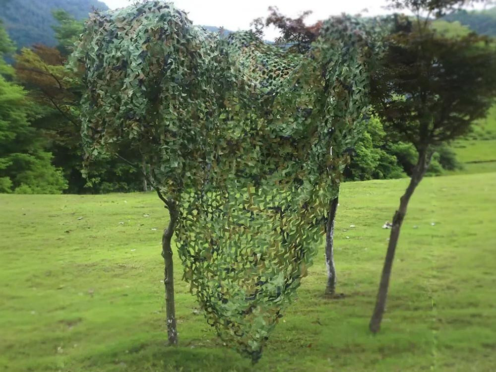 Siatka maskująca BLACK FOREST EX.24626 3 x 4 m, prywatność, altana, kemping, aranżacja, Wysoka siatka maskująca kamuflażowa przy drzewach w terenie pagórkowatym.