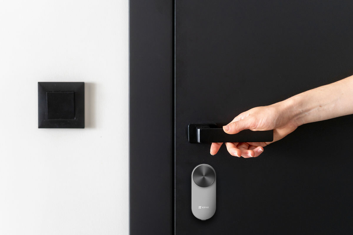 Zamek szyfrowy EZVIZ DL01 PRO+DL01CP+A3(KIT), eleganckie, wyposażenie, design, harmonijnie, dłoń chwyta za klamkę drzwi, poniżej zamontowany zamek EZVIZ
