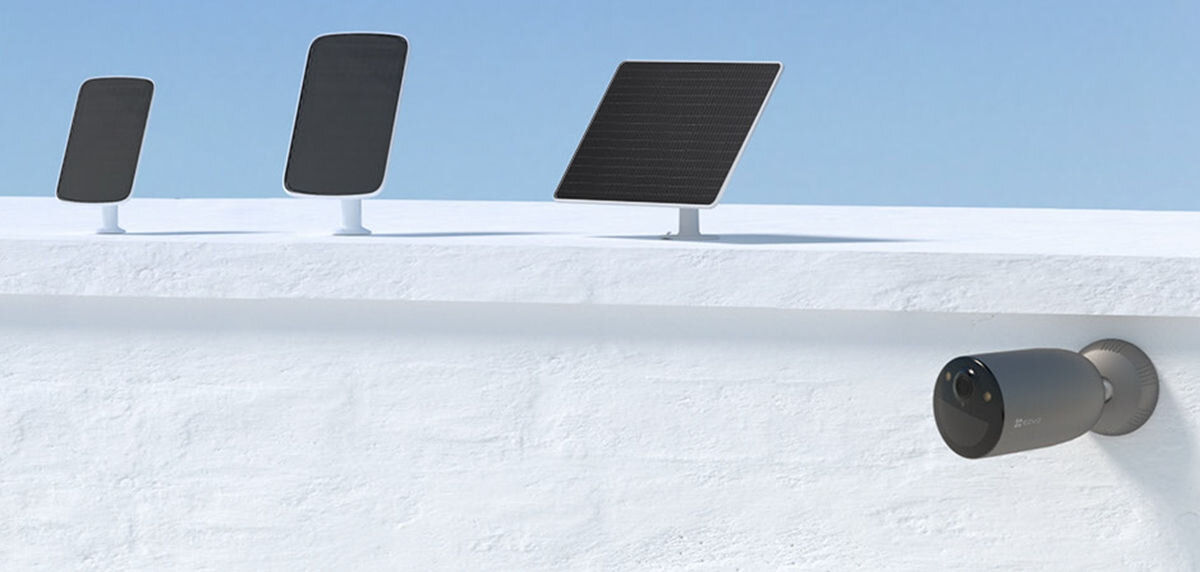 Kamera EZVIZ EB3 Zewnętrzna, 4G LTE + Panel solarny, ekologia, wygoda, ładowanie, koszty, Trzy czarne panele słoneczne na białym dachu, kamera EZVIZ zamontowana na ścianie