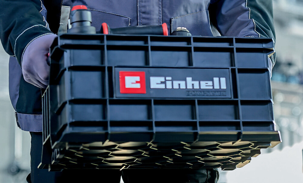 Skrzynka na narzędzia EINHELL E-Case 4540037 osoba niesie skrzynkę w dłoniach z wysokiej jakości polipropylenu odporność a uderzenia i wysoką temperaturę obciążenie do 90 kg